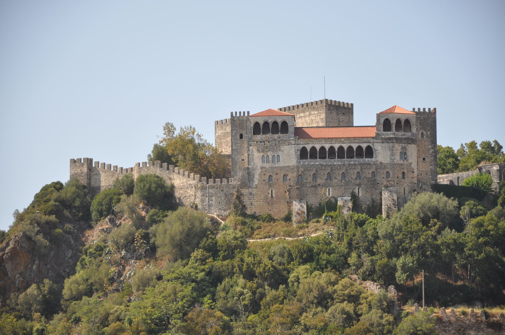 O castelo de Leiria, de pedra e com telhados vermelhos, no alto de uma colina coberta de vegetação