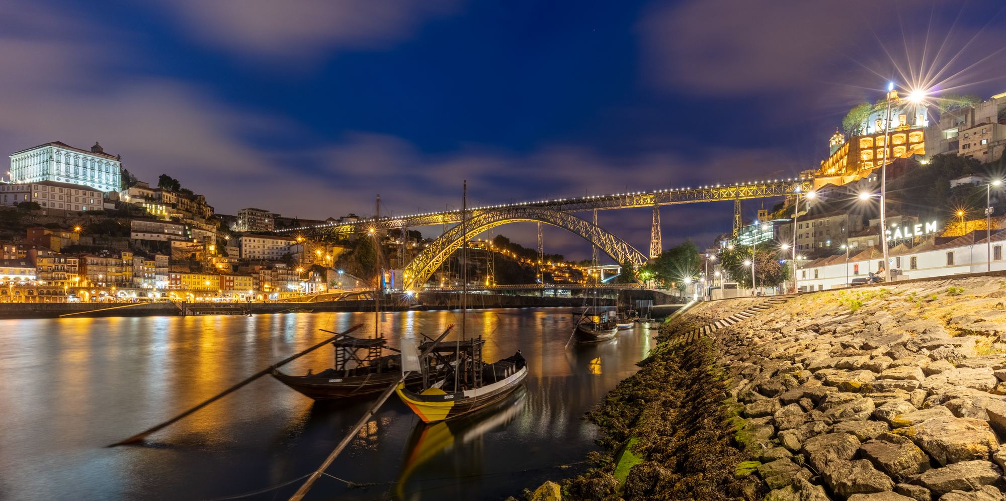 O rio Douro ao anoitecer, com barcos rabelo, a ponte Luís I iluminada e as casas da Ribeira