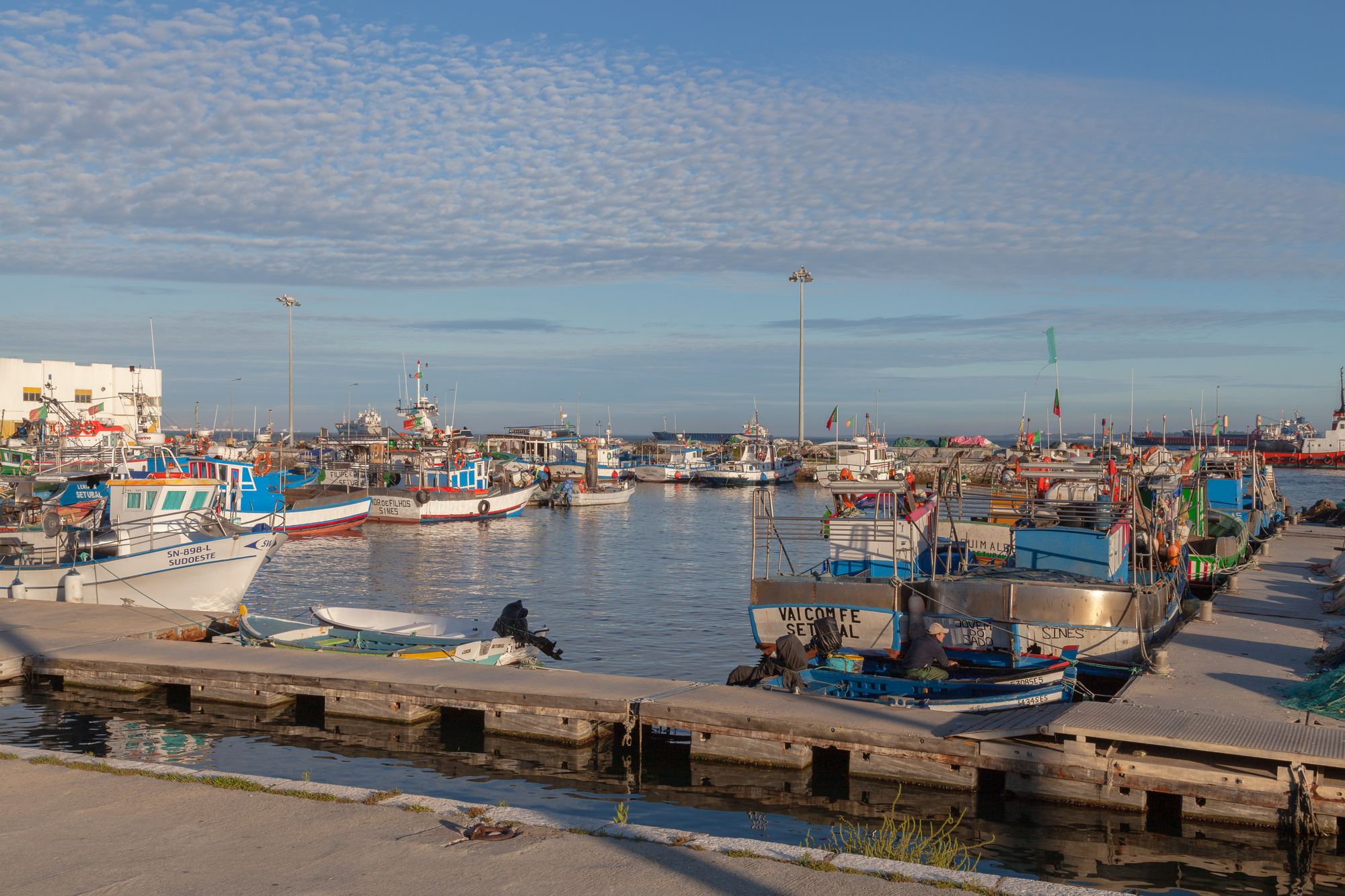 O porto de pesca de Setúbal, com barcos de pesca coloridos amarrados ao cais e um céu de nuvens pequenas
