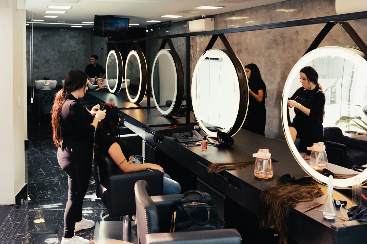 Estilistas atendiendo a sus clientas frente a los espejos de un salón de belleza