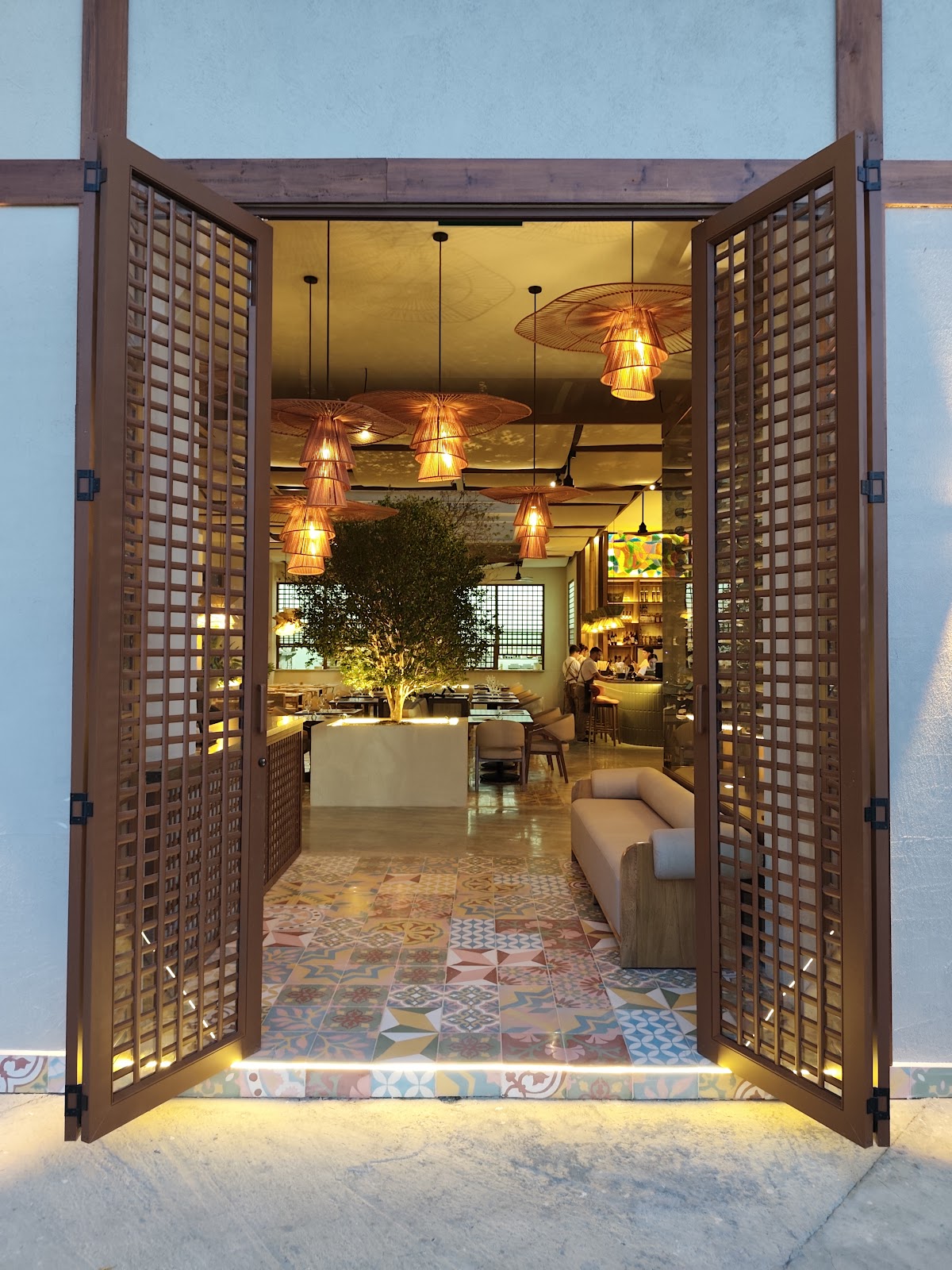 Puertas de celosía abiertas en fachada azul claro, salón iluminado y piso de baldosas