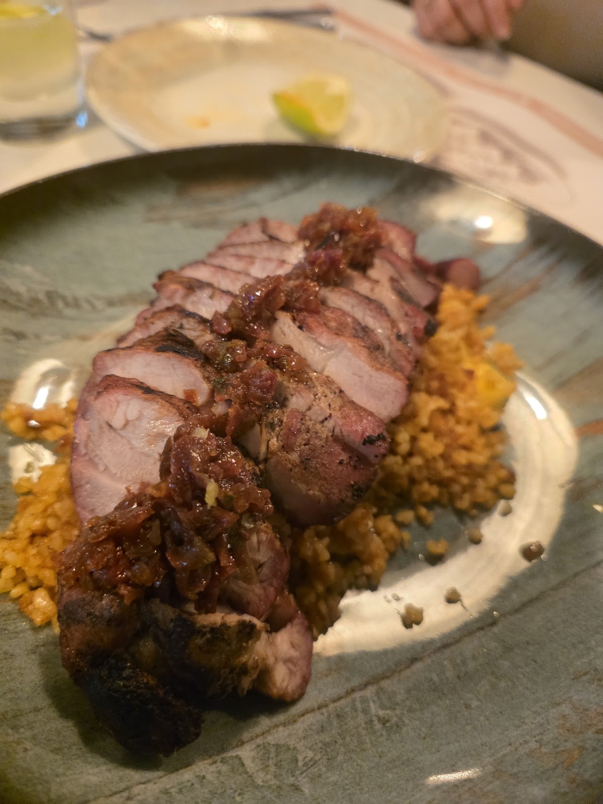 Carne asada en tajadas con salsa rojiza encima, sobre granos, en plato verde